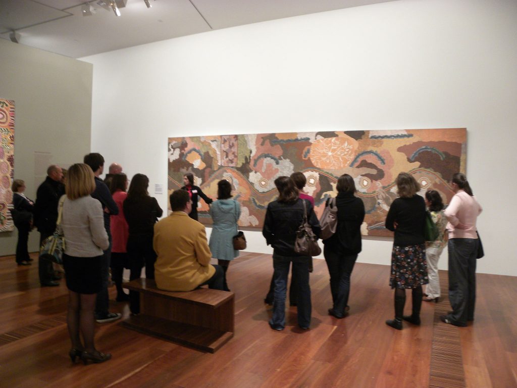 Guided Tour with IDAIA's Director and Founder, Solenne Ducos-Lamotte in front of artwork by artists Tim Leura Tjapaltjarri (Anmatyerr c.1929-1984) and Clifford Possum Tjapaltjarri (Anmatyerr c.1932-2002), Spirit Dreaming through Napperby country, 1980 – 207.7 x 670.8 cm - Synthetic polymer paint on canvas –  © the Artists © IDAIA