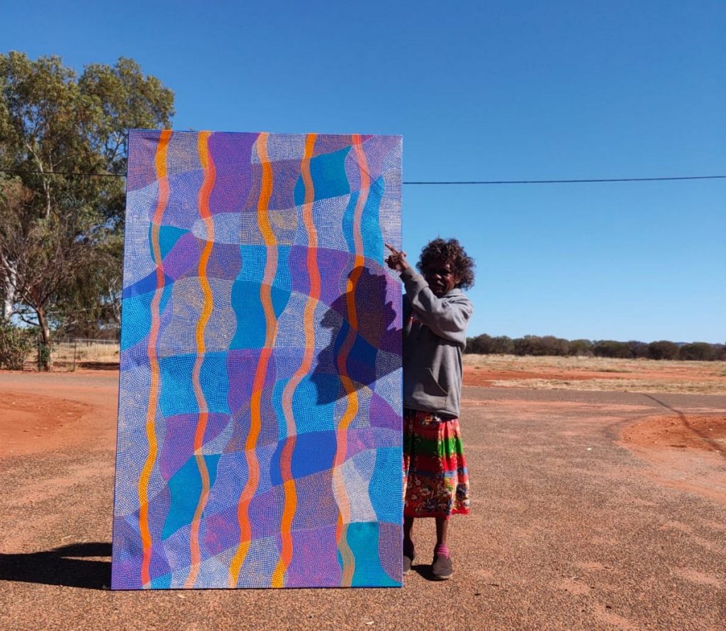 Ann Lane with her painting 'Pirrnpirrnga - Desert Bore' 2021 - 122 x 198 cm - Courtesy Ikuntji Artists - Photo Chrischona Schmidt